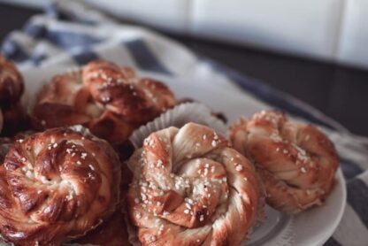 Swedish cinnamon buns on a white plate, sitting on a blue and white striped kitchen towel, white subway tiles in the background