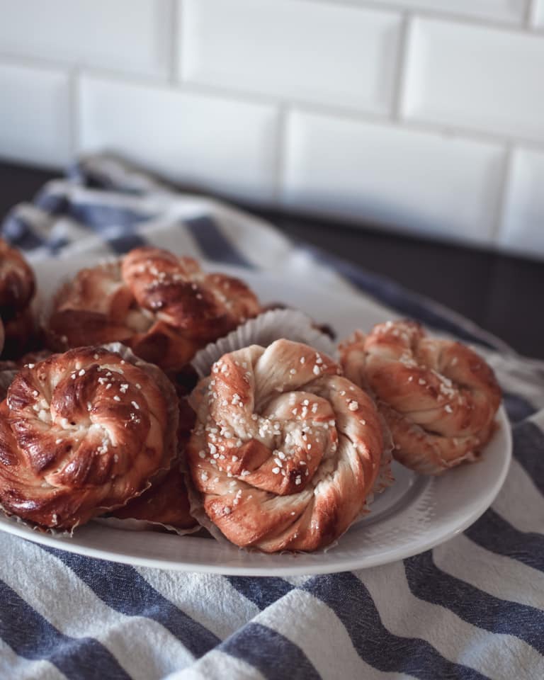 Swedish cinnamon buns on a white plate, sitting on a blue and white striped kitchen towel, white subway tiles in the background